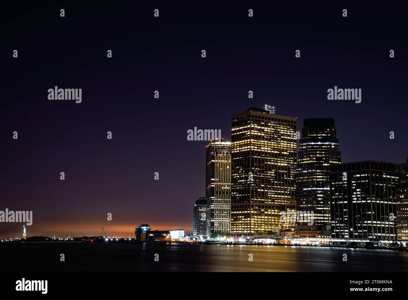 Manhattan Financial District and the Statue of Liberty seen from Brooklyn Bridge Park at Night - New York City, USA Stock Photo