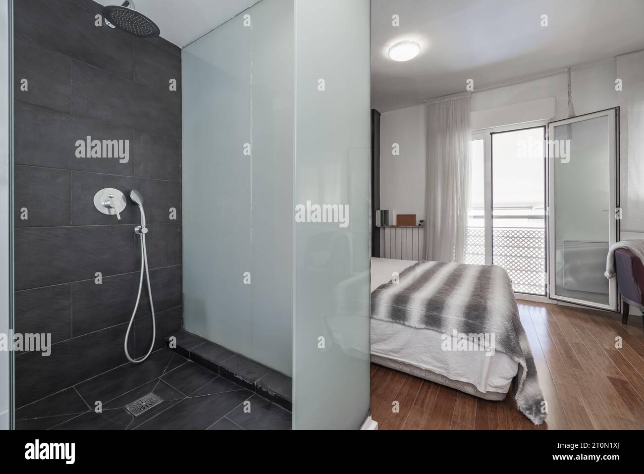 Bathroom with shower cabin with tempered glass next to an en-suite bedroom with a small balcony Stock Photo