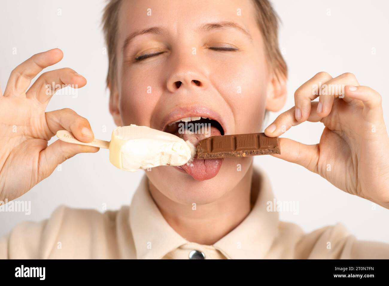 A woman with short hair indulging in ice cream and chocolate, capturing her love for sweets against a clean and simple white background Stock Photo