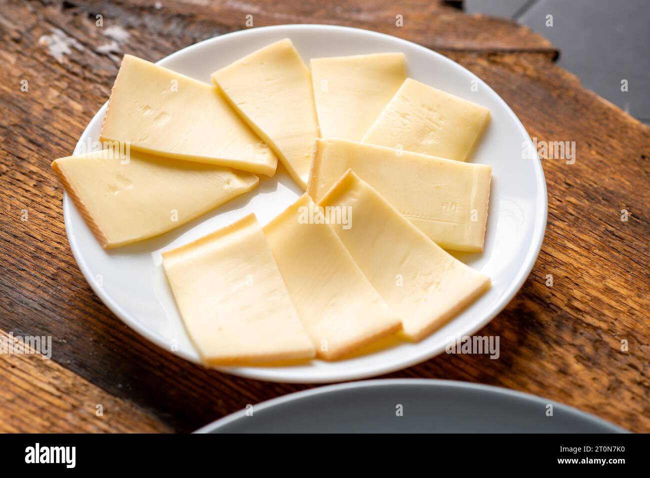Plate with slices of sliced cheese on wooden background Stock Photo