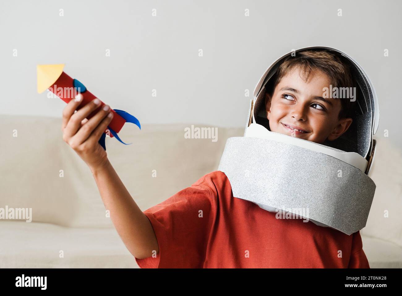 Astronaut kid playing with helmet toy and crafty rocket at home - Children imagination, moon space travel concept Stock Photo