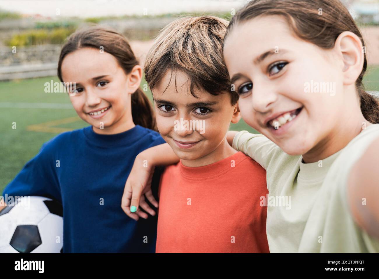 Kid friends after soccer play game having fun taking selfie in lawn - Latin children celebrating and hugging together - Childhood friendship and sport Stock Photo