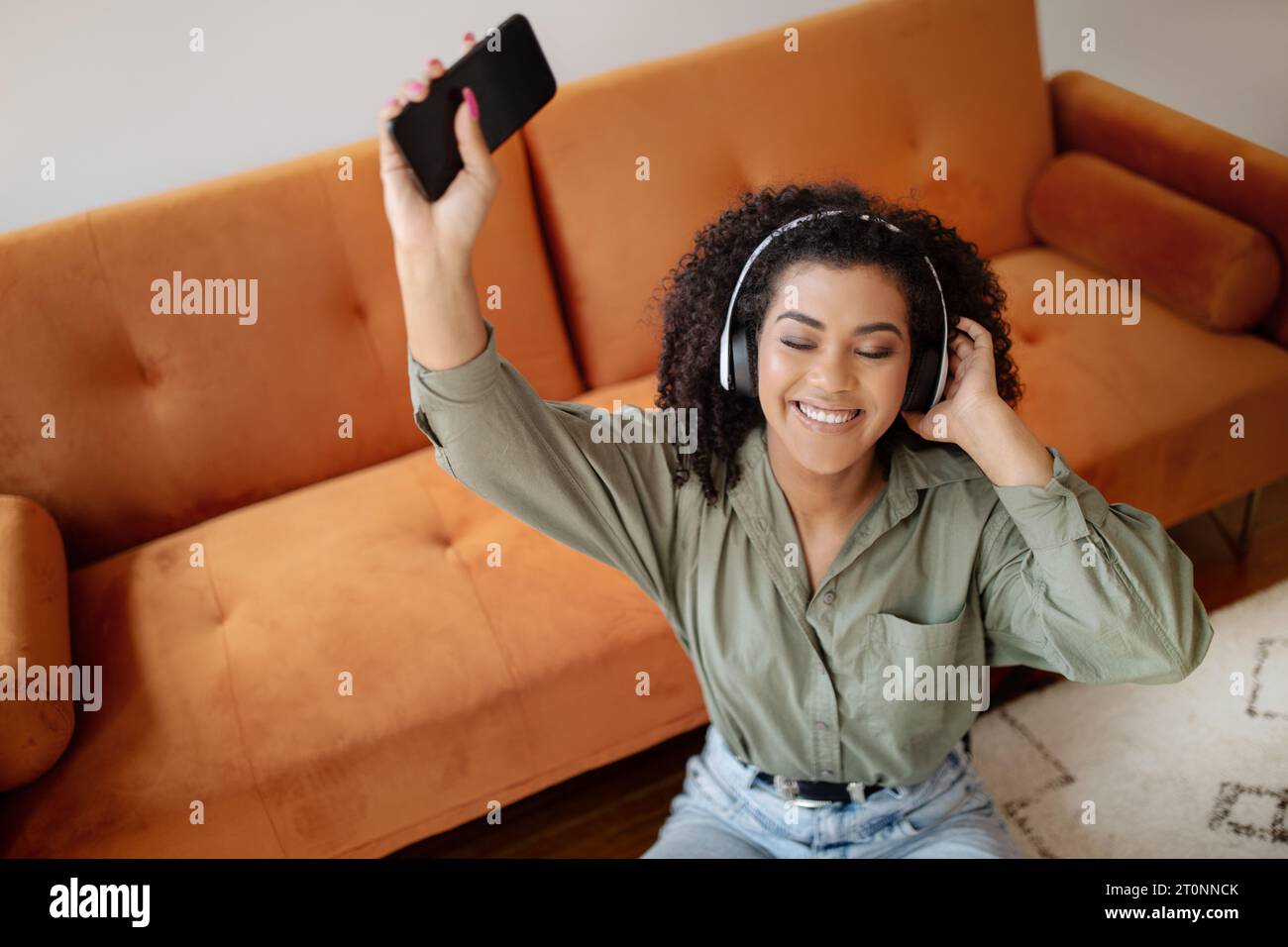 Smiling Black Lady Listening Music On Smartphone Wearing Headphones Indoors Stock Photo