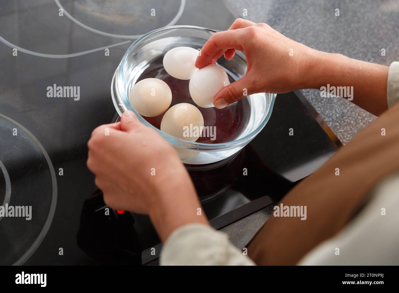 https://c8.alamy.com/comp/2T0NP9J/hands-putting-eggs-in-a-water-in-glass-pot-on-electric-stove-boiled-eggs-cooking-2T0NP9J.jpg