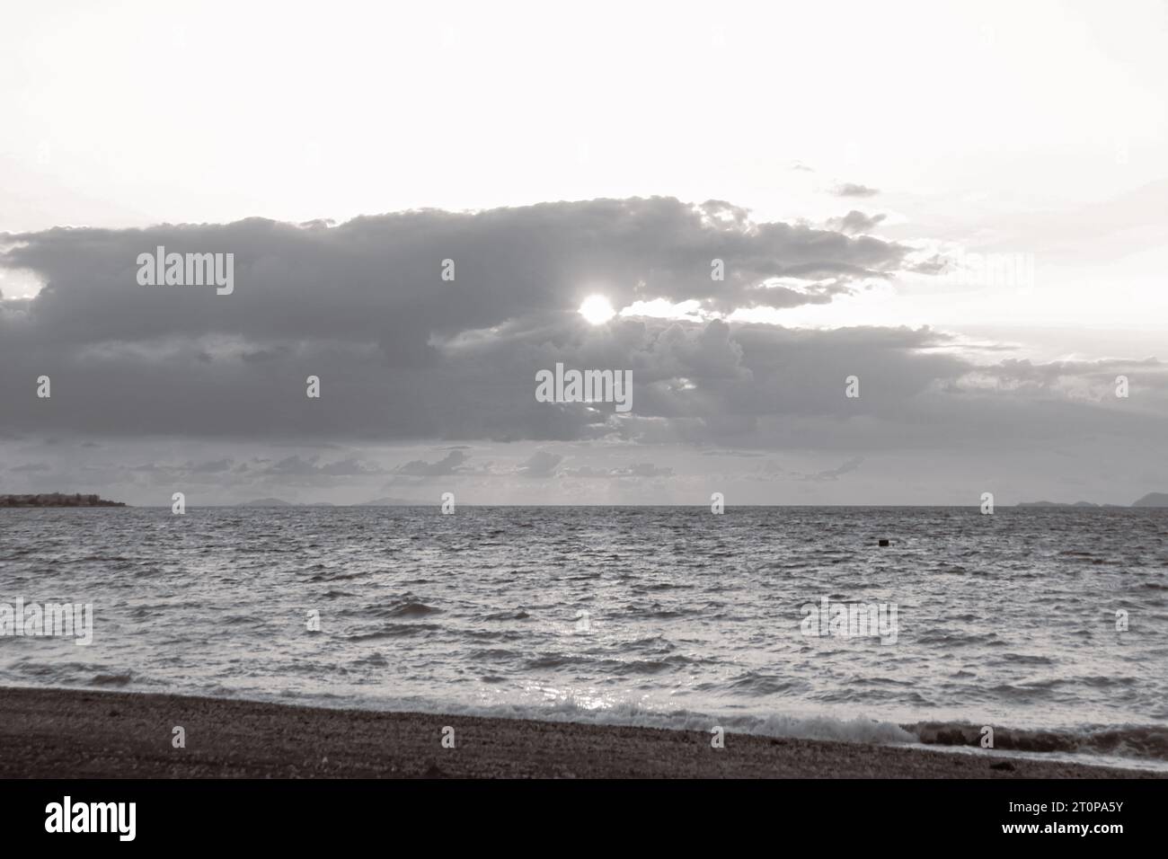 Sun shinning through the clouds at sunset at Paralia Ixia beach off Rhodes city in black and white Stock Photo