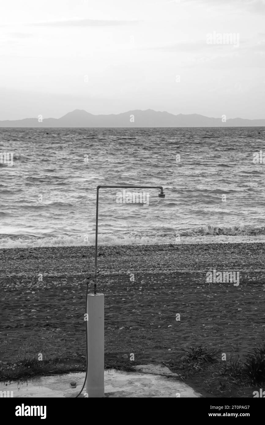 Black and white outdoor beach shower in front of the ocean at Paralia Ixia beach during sunset Stock Photo