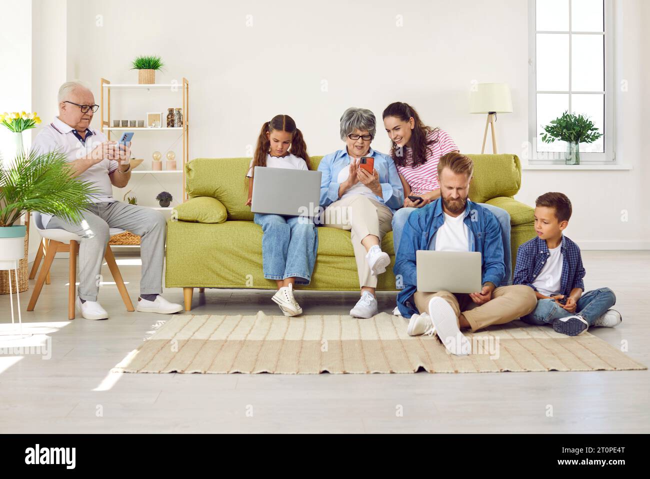 Big family sitting in living room with gadgets, parents, grandparents and two children. Stock Photo