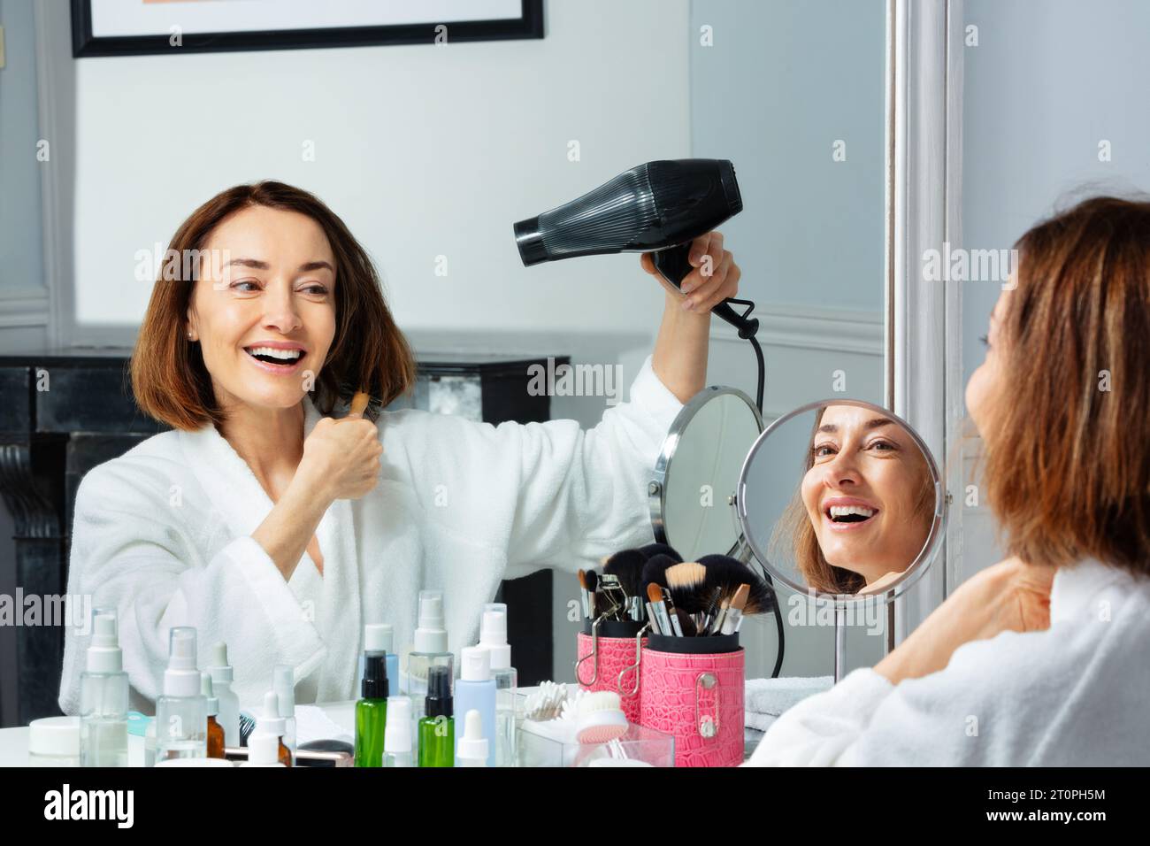 Smiling woman in housecoat holding hairdryer dry hair Stock Photo - Alamy