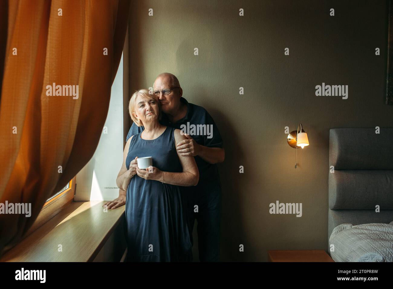 Portrait of a married elderly couple standing at the window. The man ...