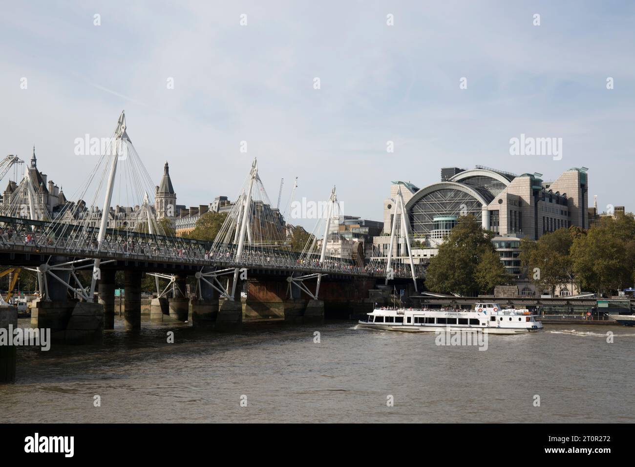 A Tourist Boat on the RiverThames Passes under Hungerford Bridge in front of Charing Cross Railway Station Westminster London Stock Photo
