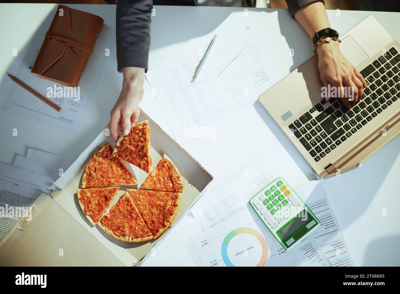 Sustainable workplace. Upper view of woman worker in green office with pizza and laptop. Stock Photo