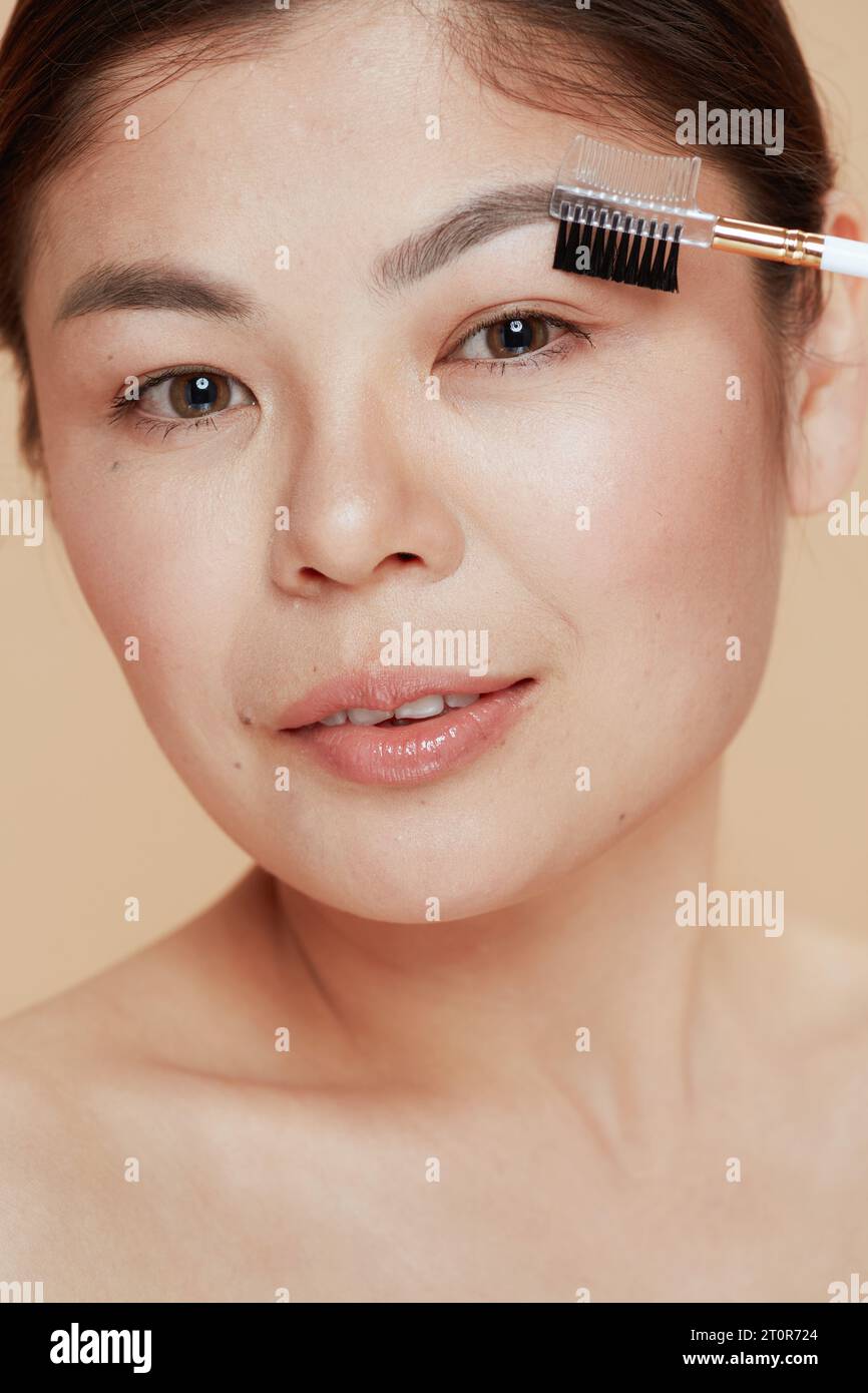 modern asian female with brow brush against beige background. Stock Photo