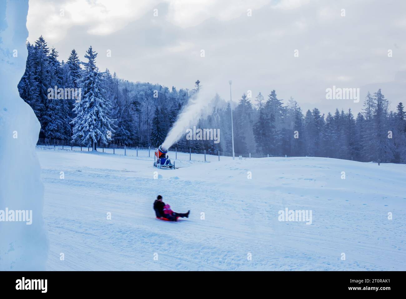Pap and child sledding in Zakopane ski resort and a snow cannon makes