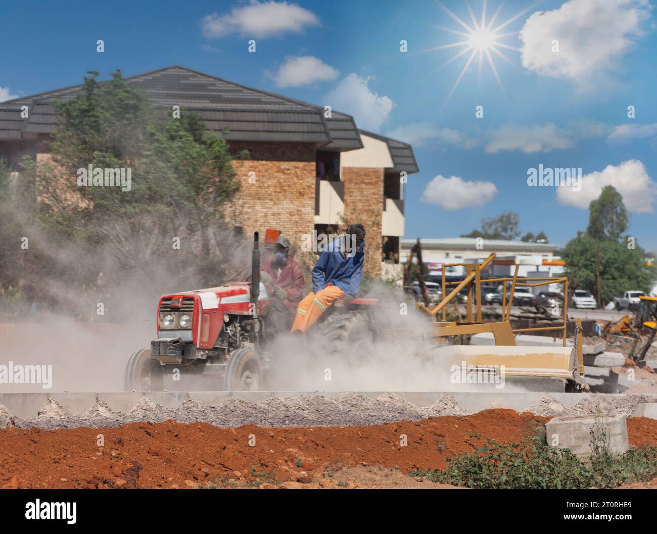 two african men on a tractor pulling a plug on a construction site between buildings with flats Stock Photo