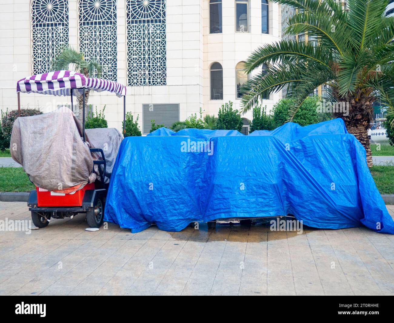 Vehicles at the resort are covered with tarps. Bicycles and scooters at the resort. The concept of the end of the holiday season. Rain protection. Bus Stock Photo