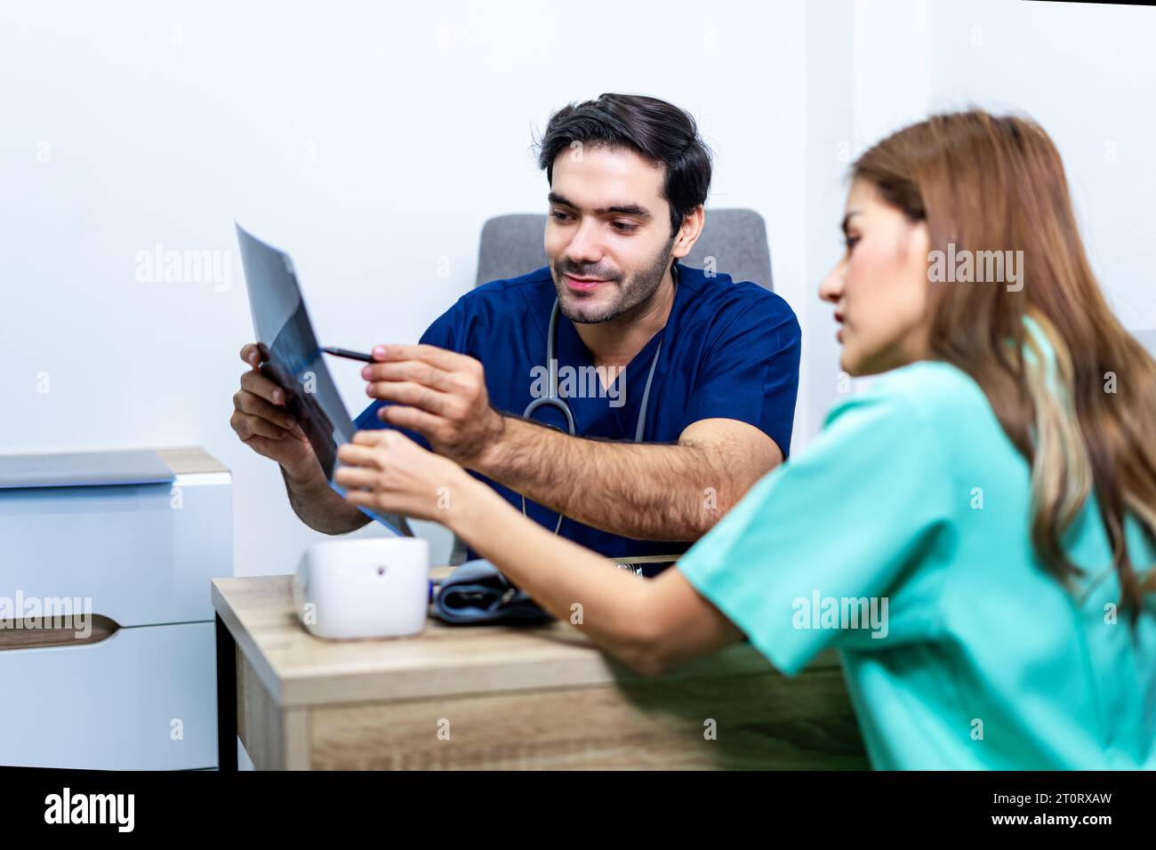 Physician men talking and looking at X Ray film with woman patient at clinic. Doctor discussing with patient in medical room at hospital. Stock Photo