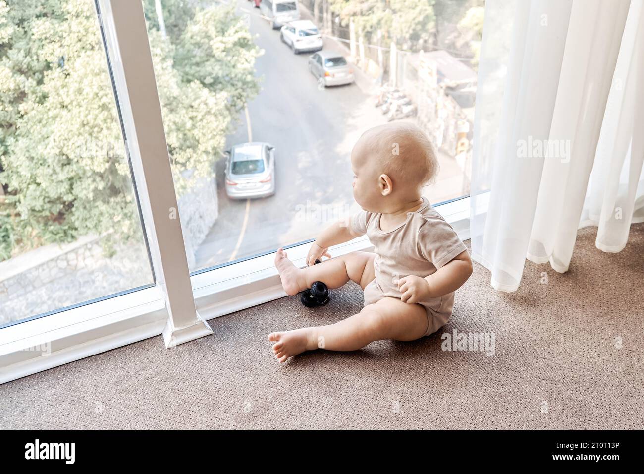Curious baby looks out of panoramic window sitting on floor. Adorable
