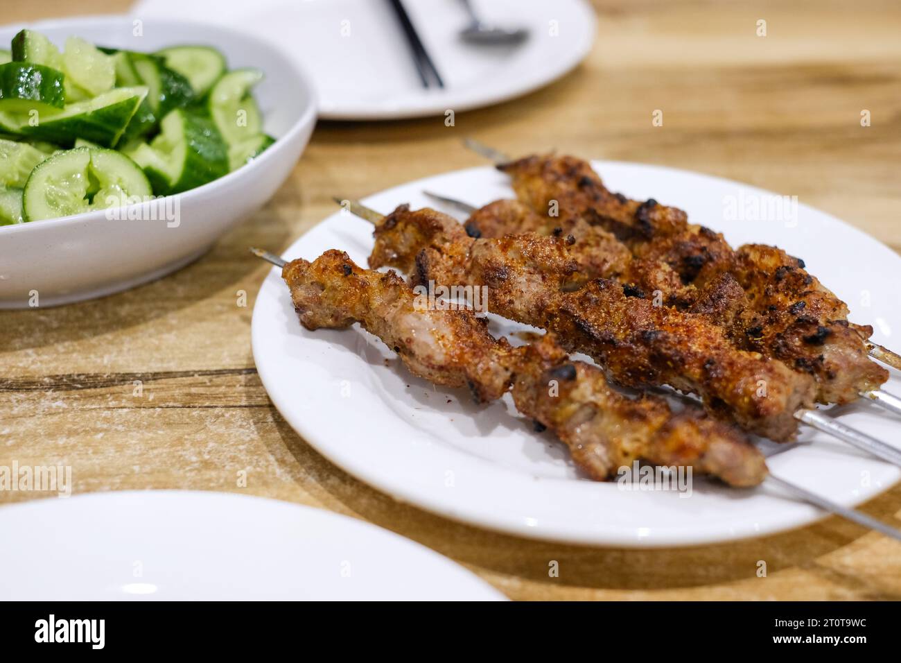 A plate of cumin lamb skewers and side dish of cucumber garlic salad at