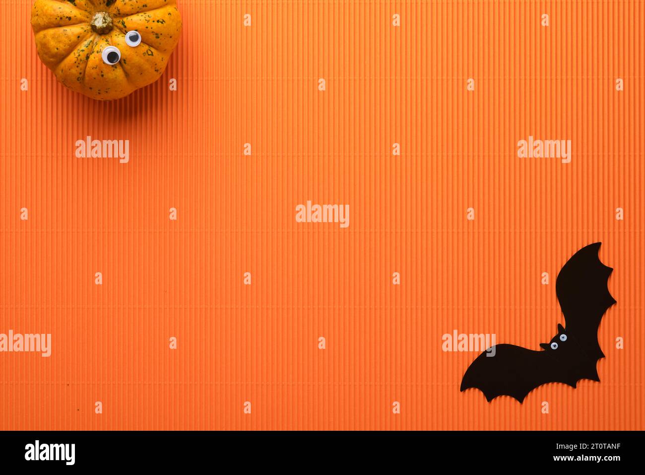 Halloween holiday background. Orange pumpkin, bat with funny eyes, spider, spider web, old leaves and branches from scary forest on orange background. Stock Photo