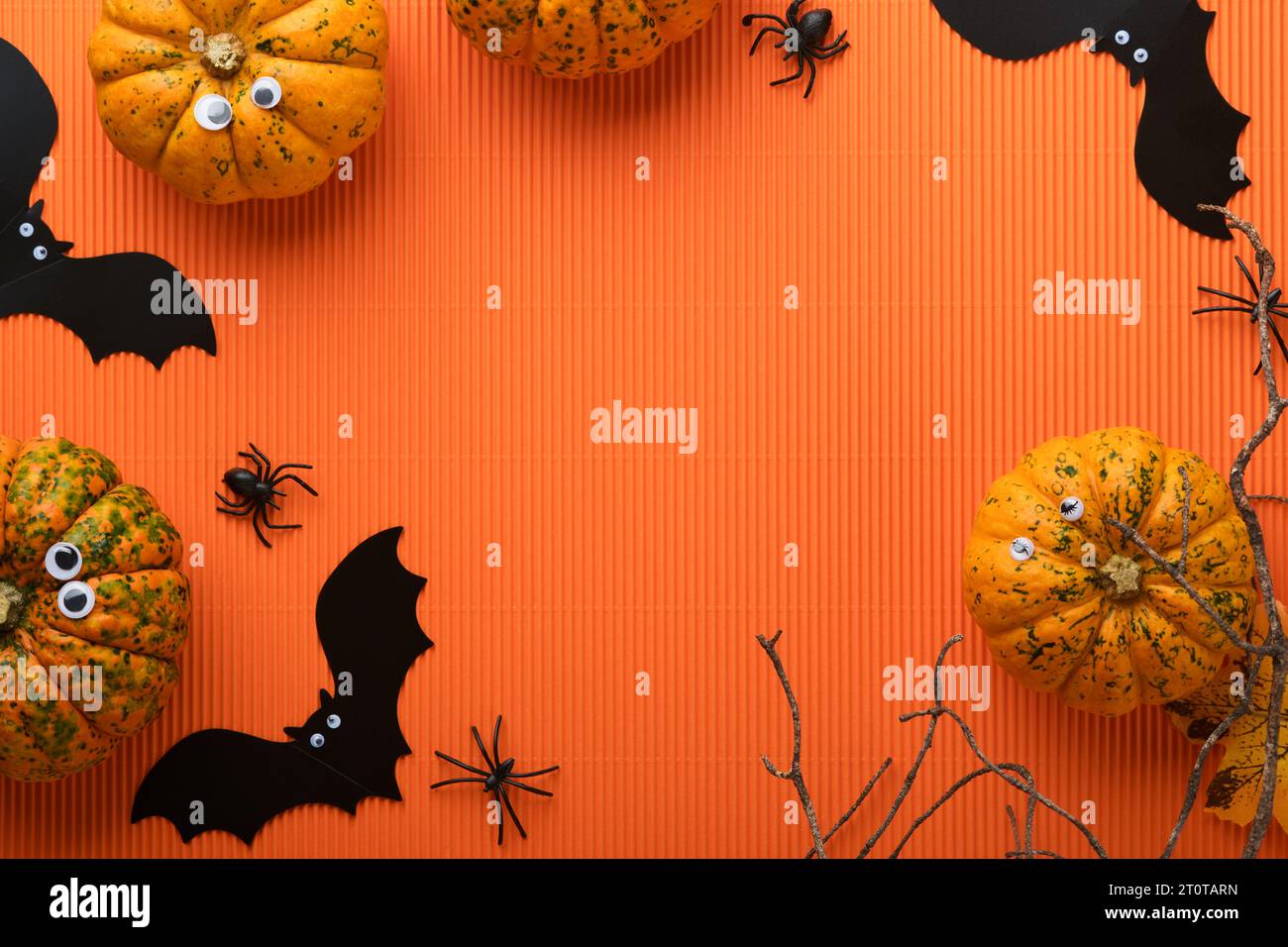 Halloween holiday background. Orange pumpkin, bat with funny eyes, spider, spider web, old leaves and branches from scary forest on orange background. Stock Photo