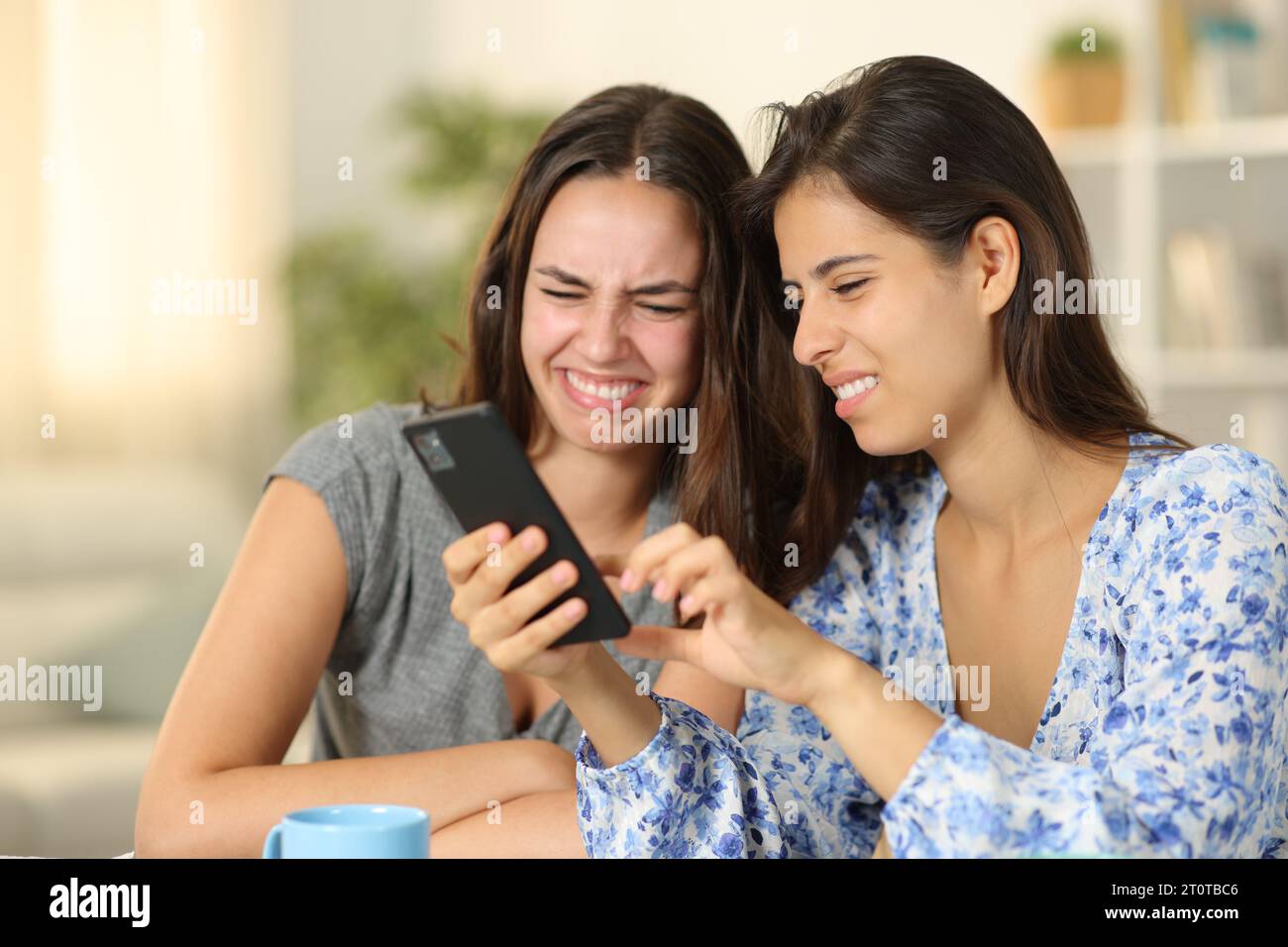 Disgusted women checking nasty cell phone content at home Stock Photo