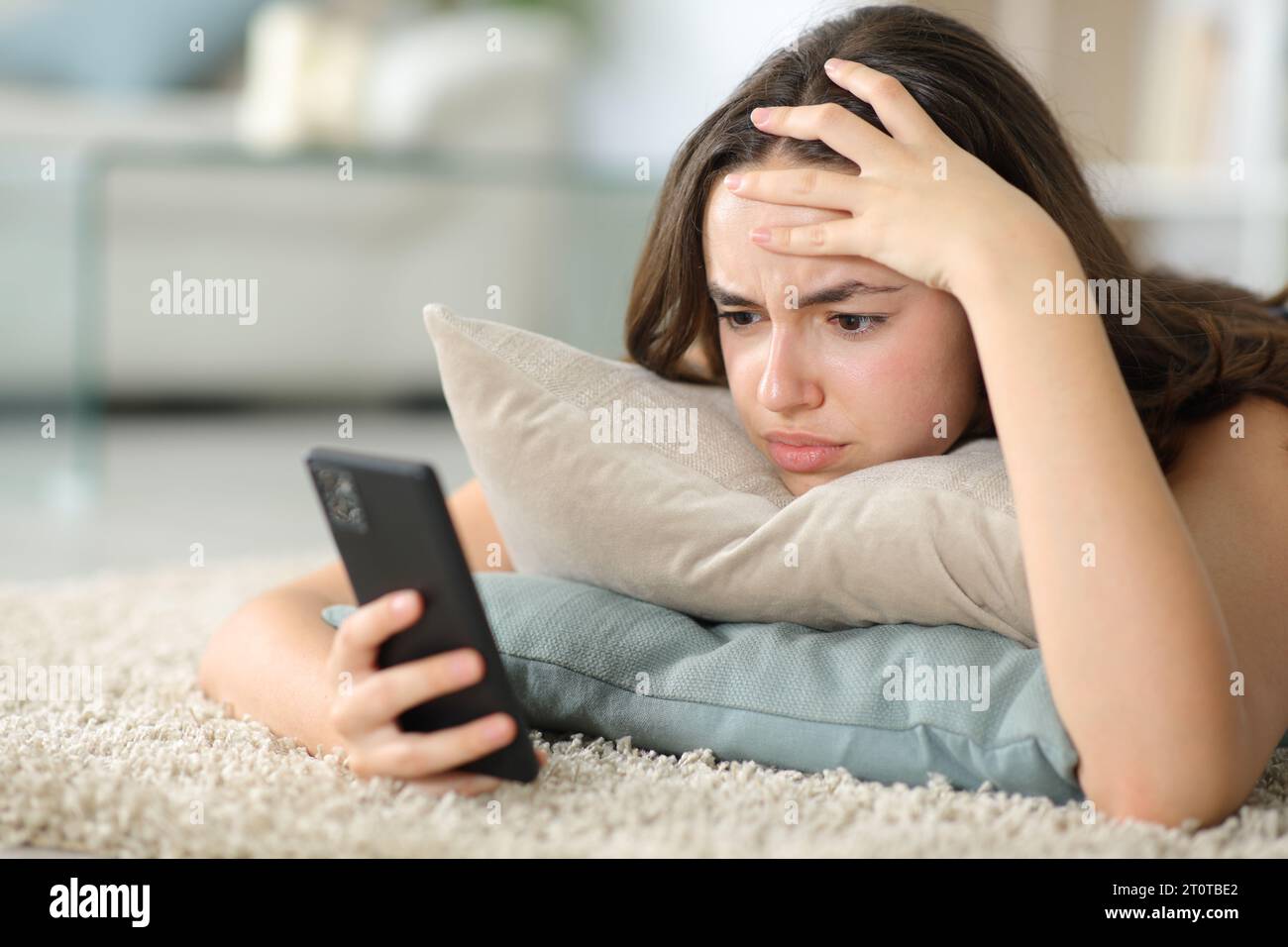 Worried woman checking phone lying on the floor at home Stock Photo