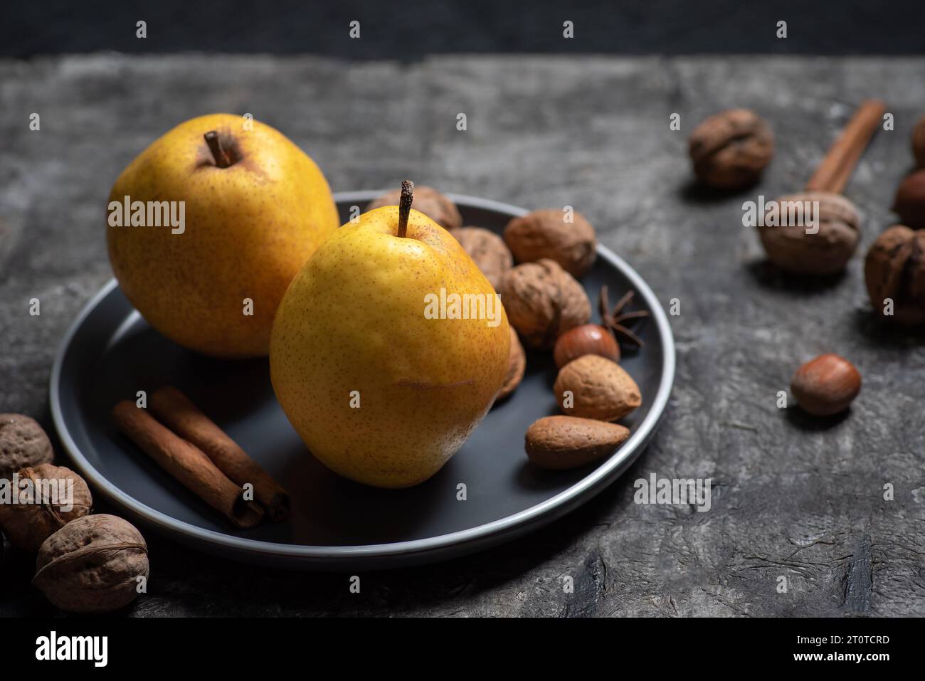 Two fresh, organic yellow pears in a bowl with nuts on a dark wooden background Stock Photo