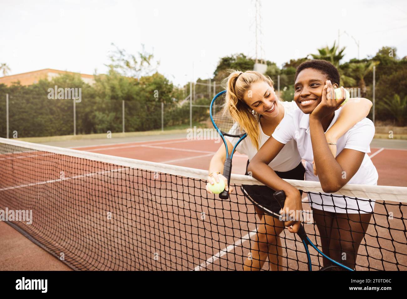 Portrait of two young beautiful women with tennis clothes and rackets in a tennis court ready to play a game. Stock Photo