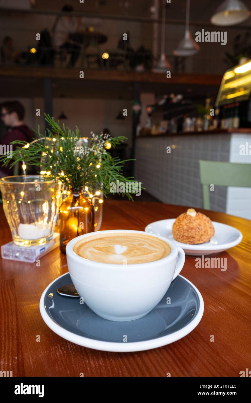 Freshly served cup of cappuccino and a japanese shu cream on a wooden table in a cafe. Stock Photo