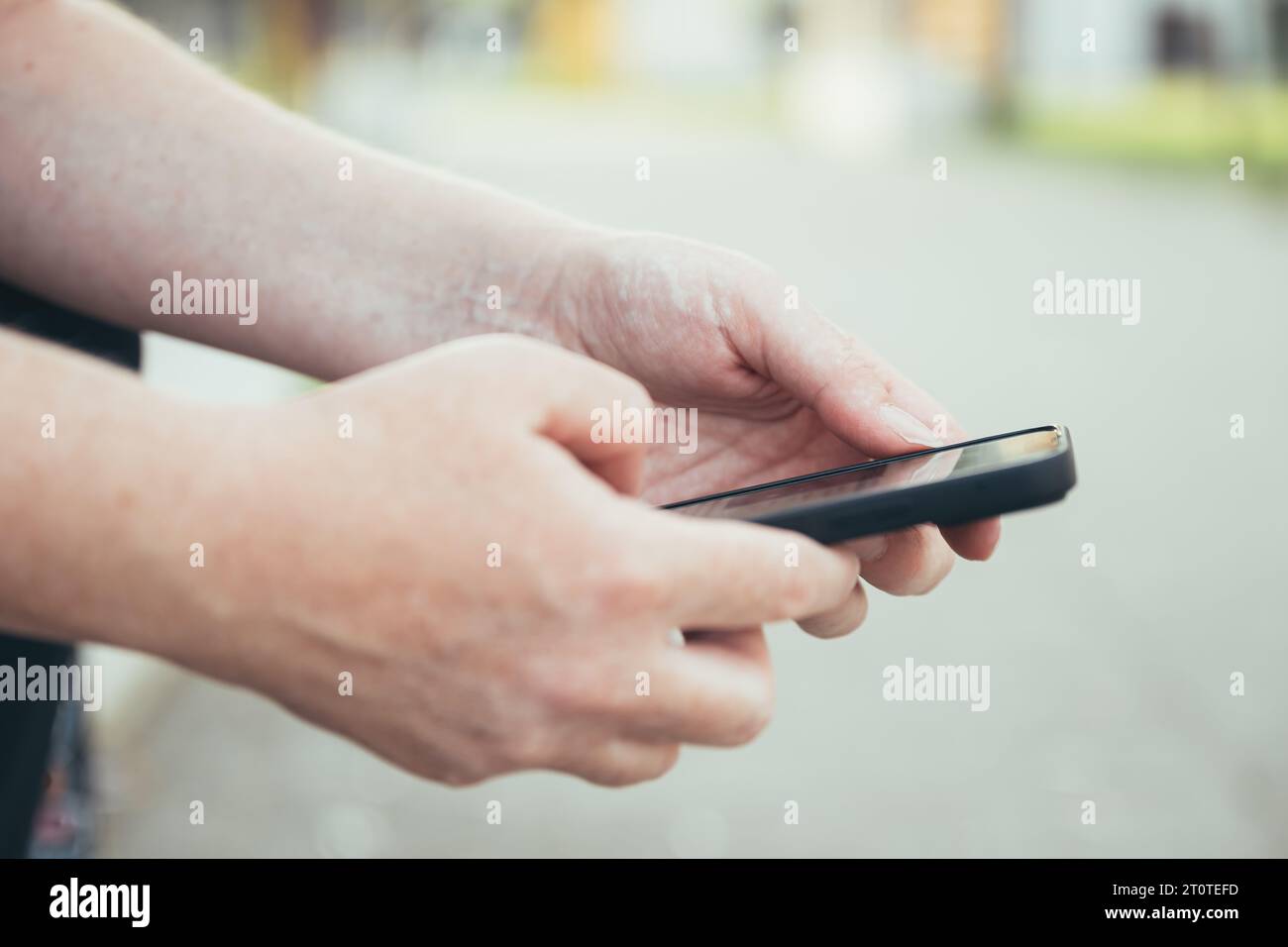 Woman browsing the internet on mobile phone while sitting on the bench in public park, closeup of hands with selective focus Stock Photo