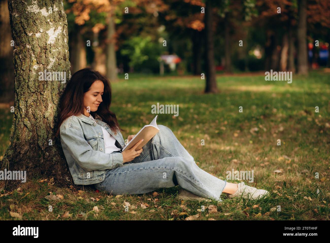 Young woman reading book under the tree during picnic in evening sunlight. High quality photo Stock Photo