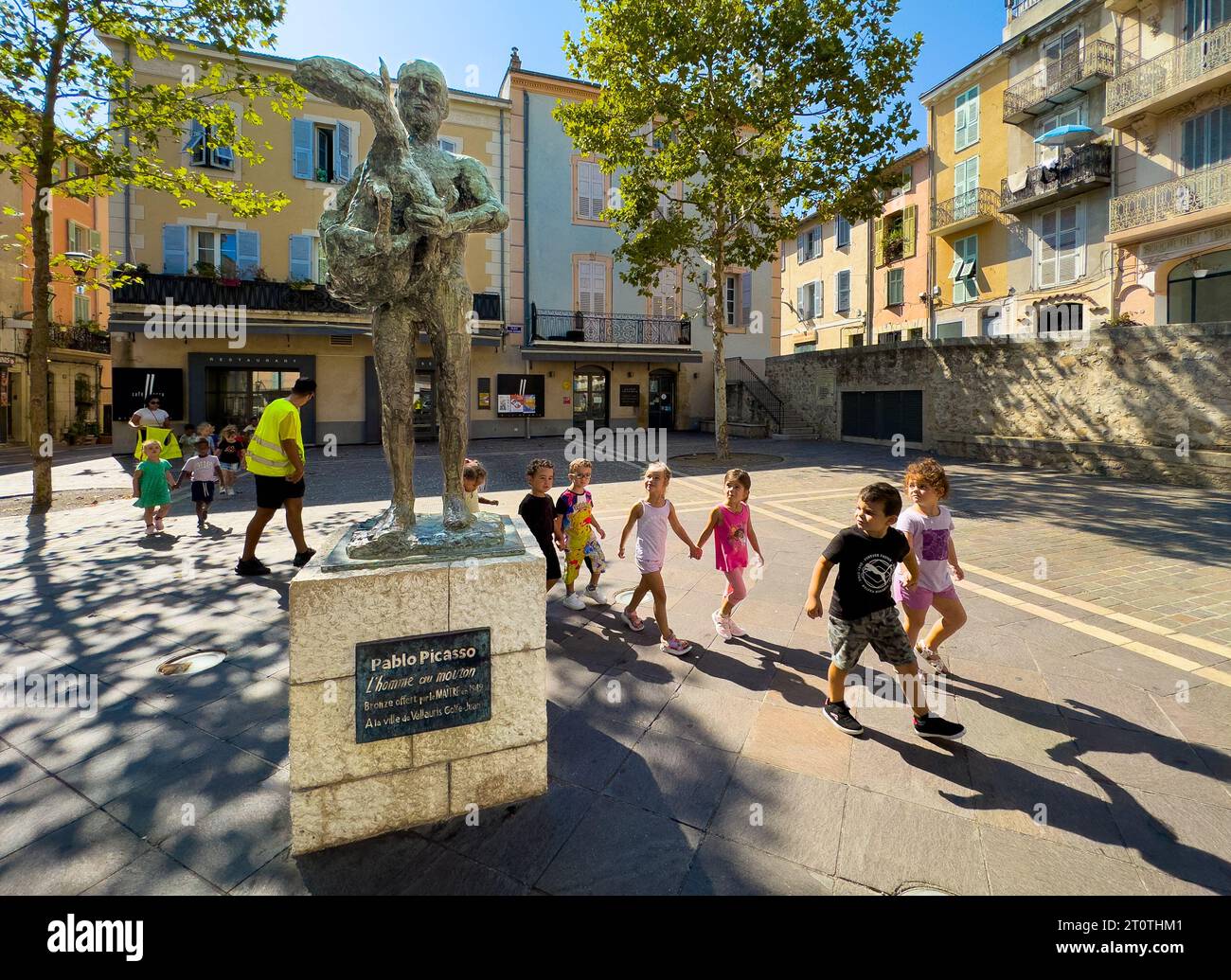 Children walk past 'Man with a Sheep' (L'homme au mouton)', bronze statue by Pablo Picasso gifted by the artist in 1949 to the town of Vallauris, Alpe Stock Photo