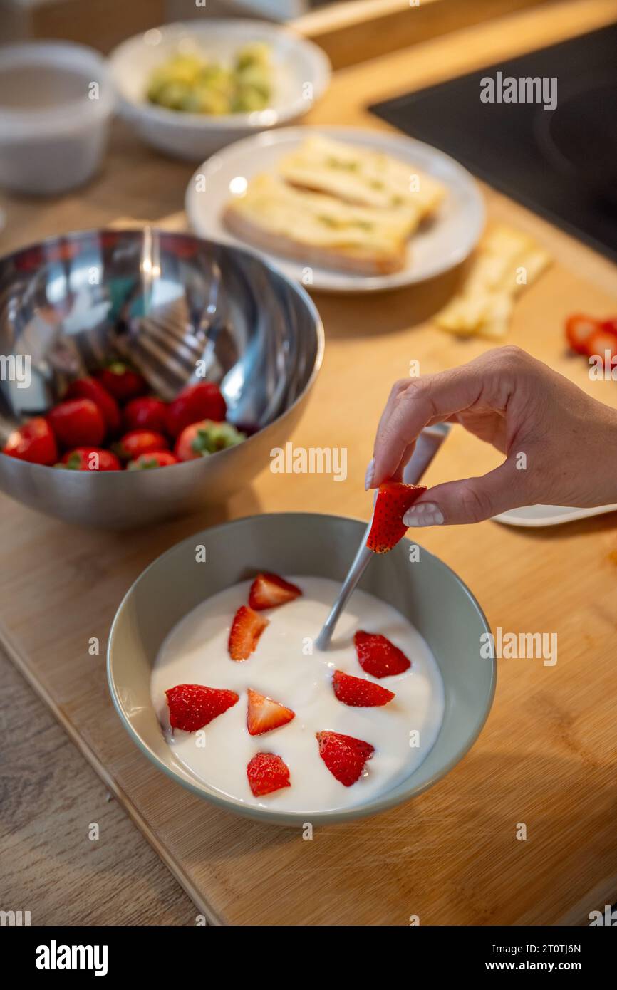 Crop view of a hand making a healthy breakfast meal with plain yogurt and strawberries on kitchen counter Stock Photo