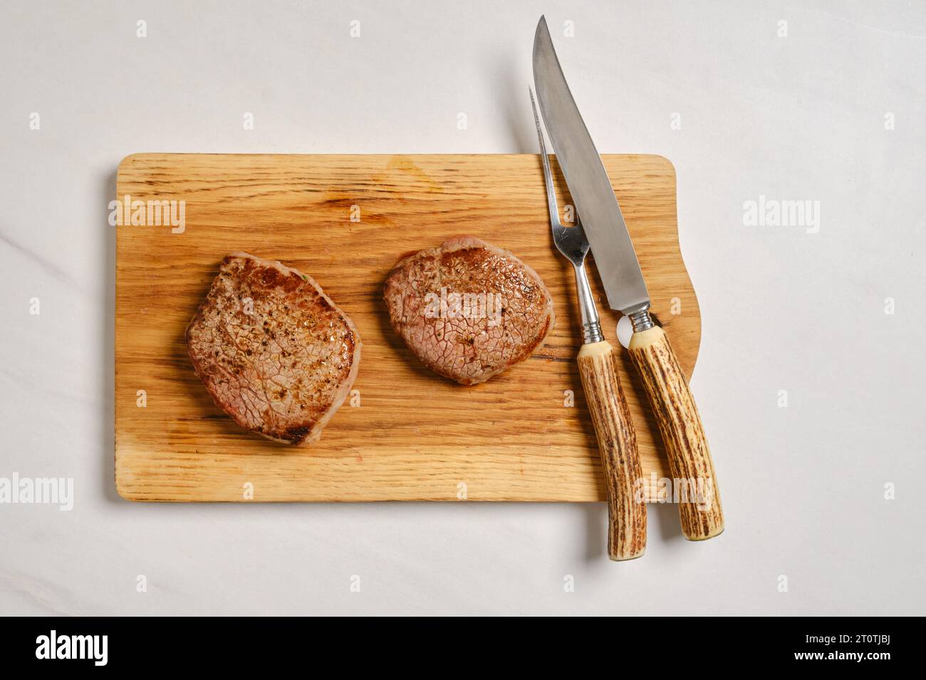 Top view of juicy beef steak on wooden cutting board next to fork and knife Stock Photo