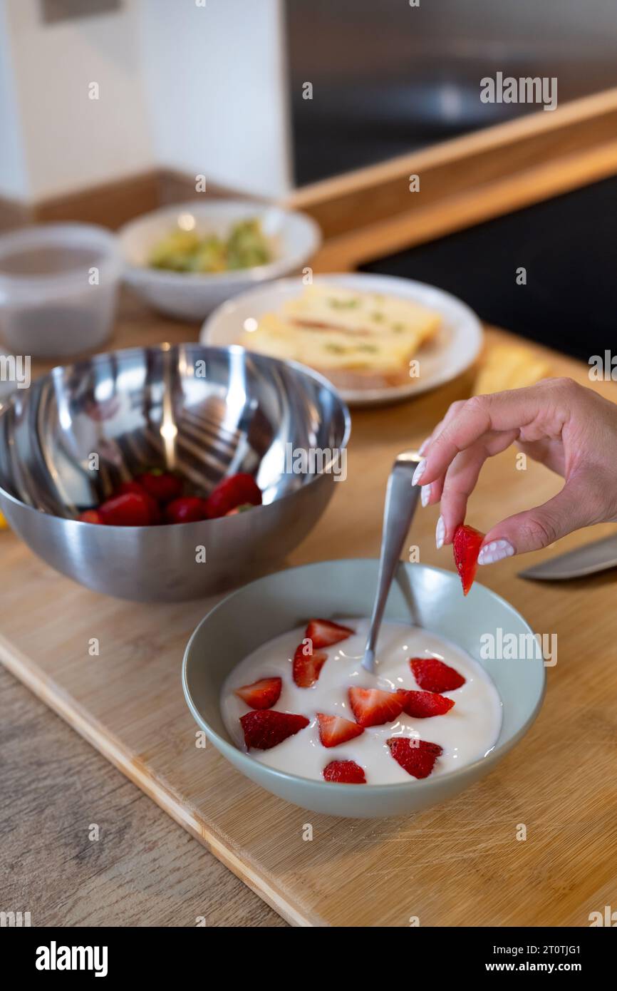 Crop view of a hand making a healthy breakfast meal with plain yogurt and strawberries on kitchen counter Stock Photo