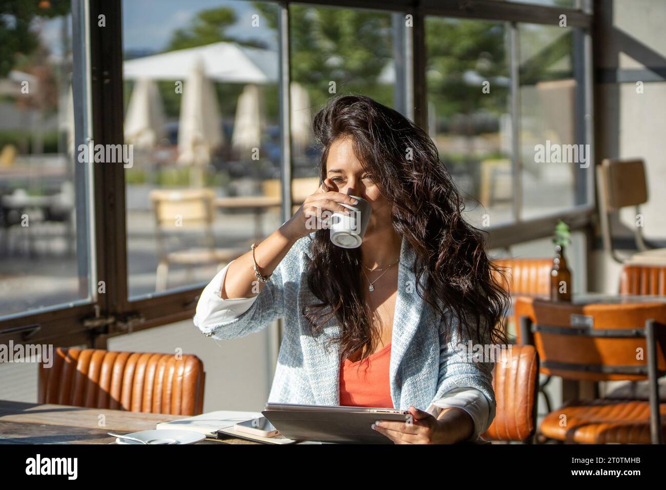 Woman drinking coffee and holding a digital tablet while sitting in coffee shop. Technology concept. Stock Photo