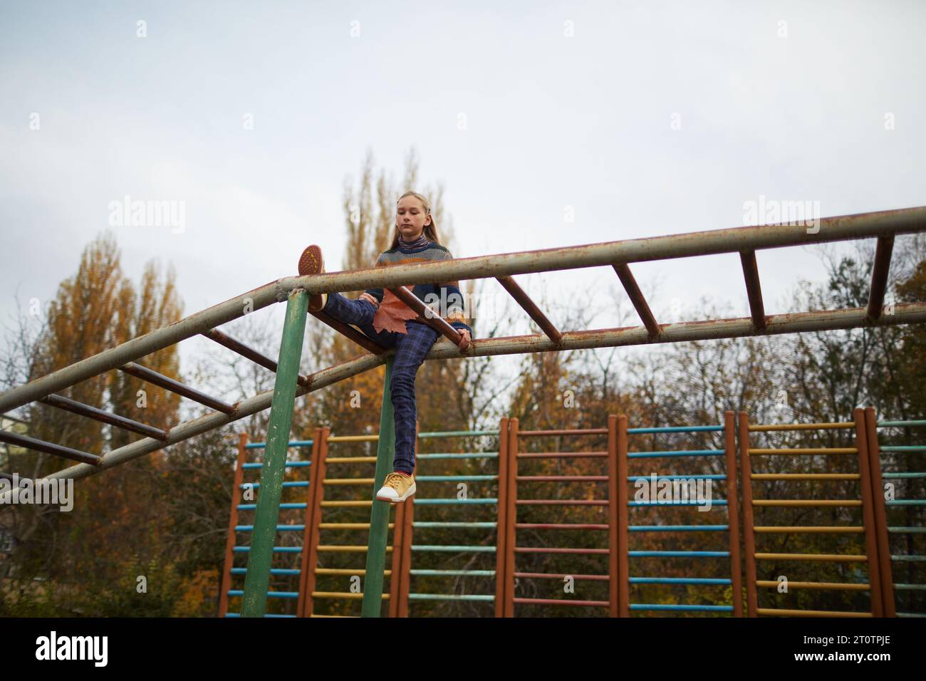 calm teenage girl sitting on monkey bars at playground Stock Photo
