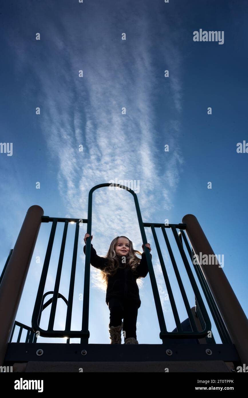 Little girl playing on playground under blue skies Stock Photo