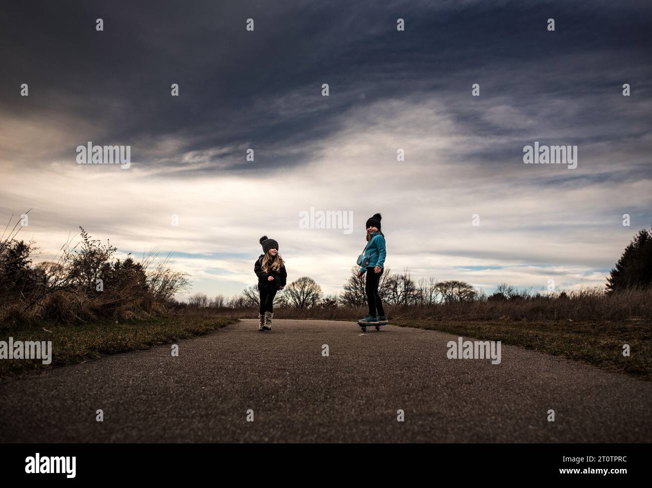 Sisters skateboarding under blue sky Stock Photo