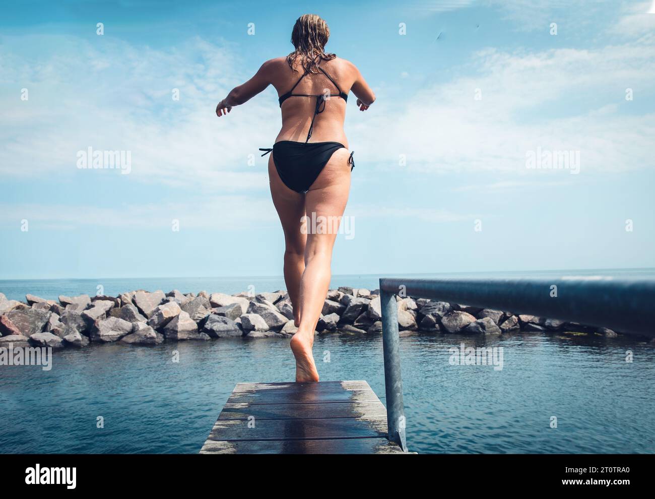 Woman Walking A Diving Board Into The Ocean In Scandinavia Stock Photo