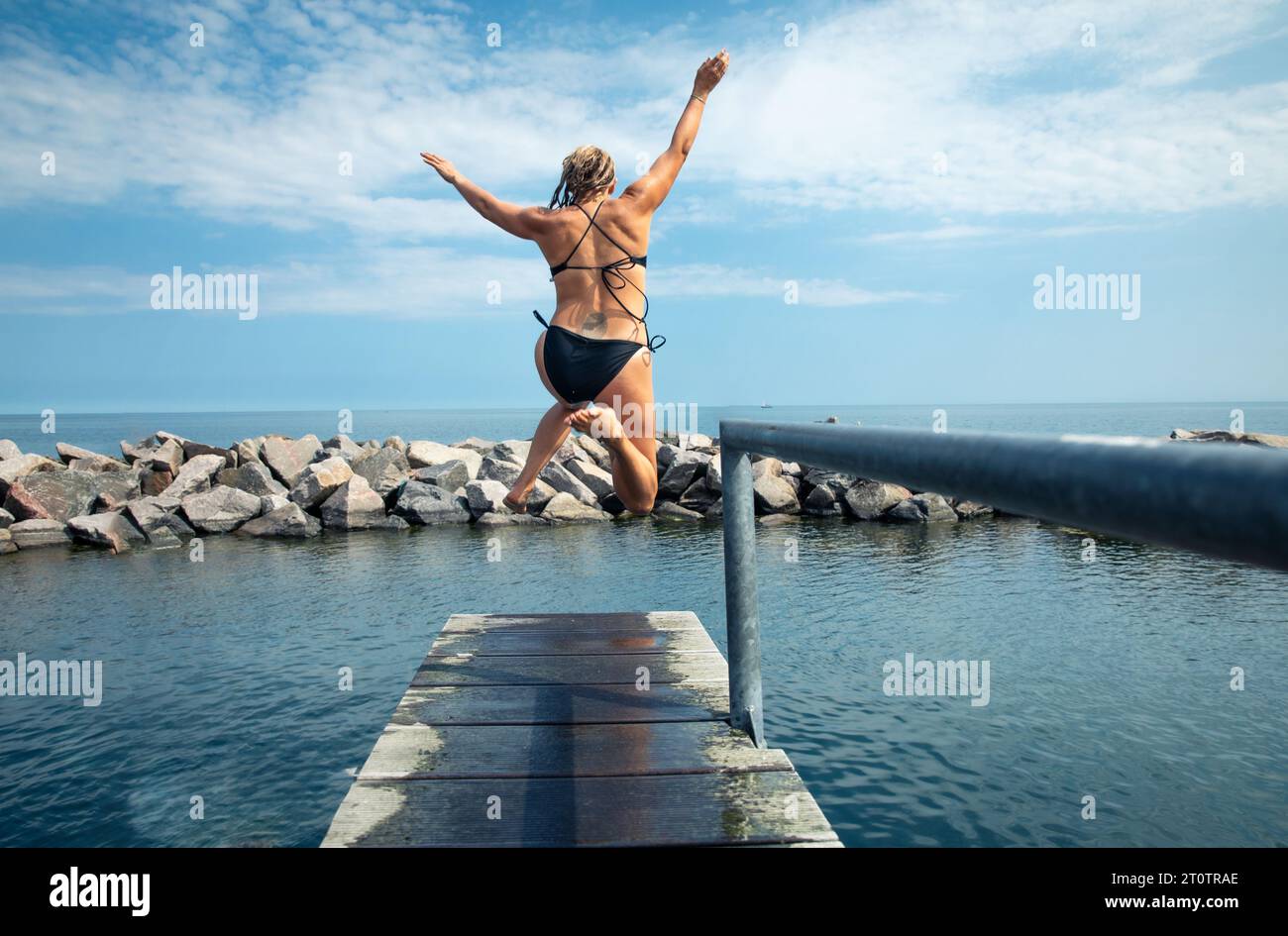 Woman With Arms and Legs In The Air Jumping Into Ocean In Denmark Stock Photo
