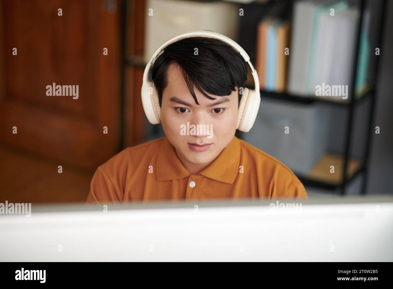 Young Asian software developer wearing headphones when working on computer in home office Stock Photo