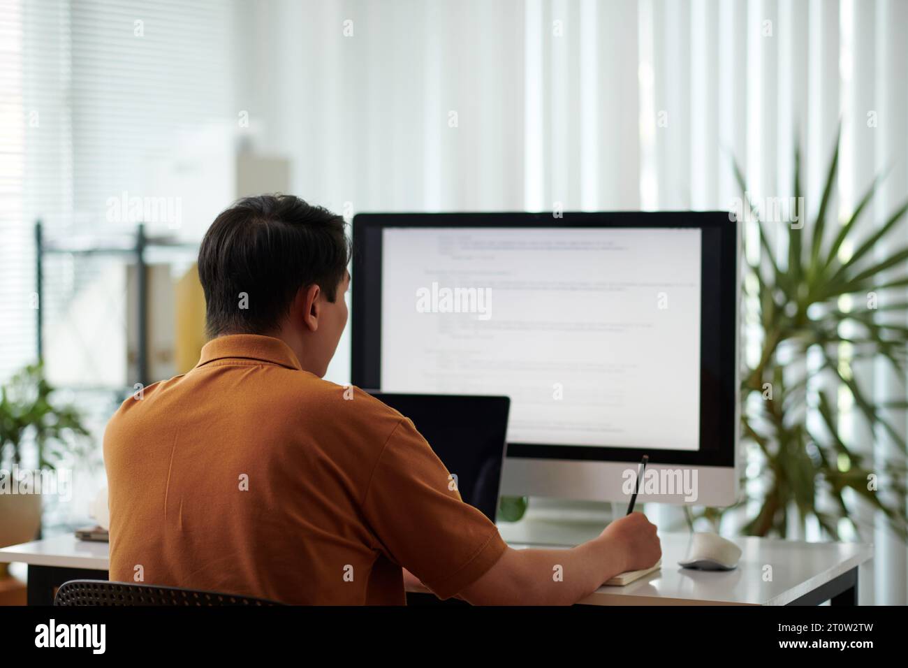 Software developer reviewing programming code and taking notes in planner Stock Photo