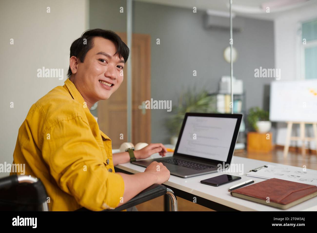 Cheerful young man with disability working on computer in office Stock Photo