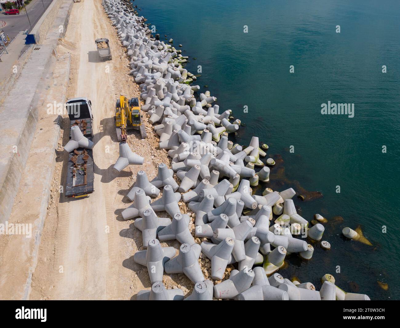 An excavator diligently constructs a dock or breakwater in the sea, its ...
