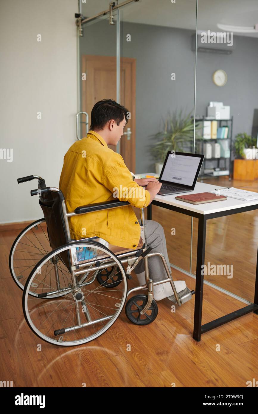 Young man with disability coding on laptop in modern office Stock Photo