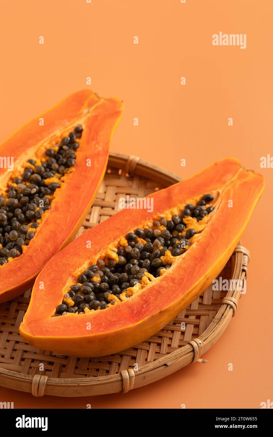 Fresh cut papaya fruit over orange table background for tropical gourmet design concept. Stock Photo