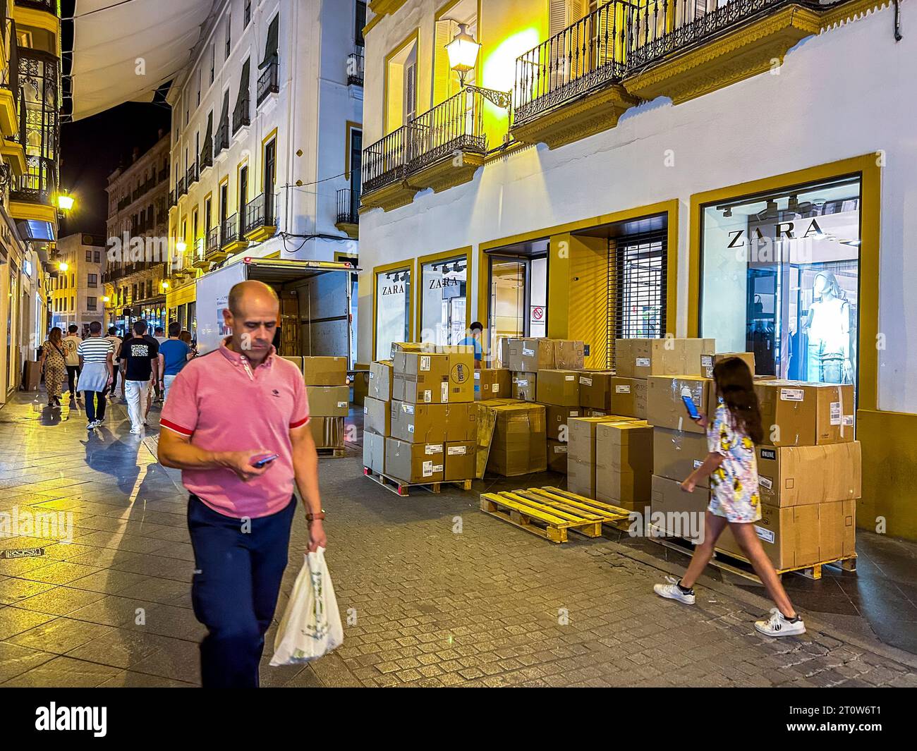 Seville, Spain, Street Scene, Fast Fashion Clothing Industry, UnLoading Boxes at Night, Zara Company, Man WaLking in Front looking at Smart Phone Stock Photo