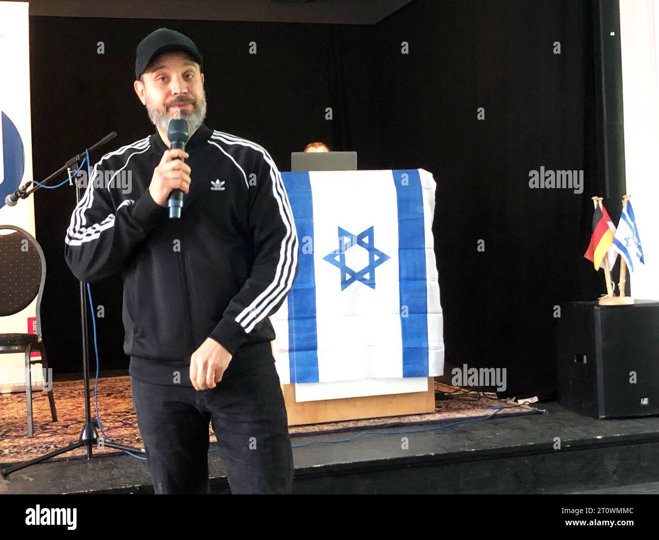 09 October 2023, Brandenburg, Oranienburg: Ben Salomo, Israeli-born rapper and speaker on anti-Semitism, speaks in front of an Israeli flag during a lecture to schoolchildren. The discussion at the start of the Israel Week of the German-Israeli Society Berlin and Brandenburg was overshadowed on Monday by the attack of the Islamist Hamas on Israel. (to dpa: 'Rapper Solomon: Anti-Semitism in Germany faded out for too long') Photo: Monika Wendel/dpa Stock Photo