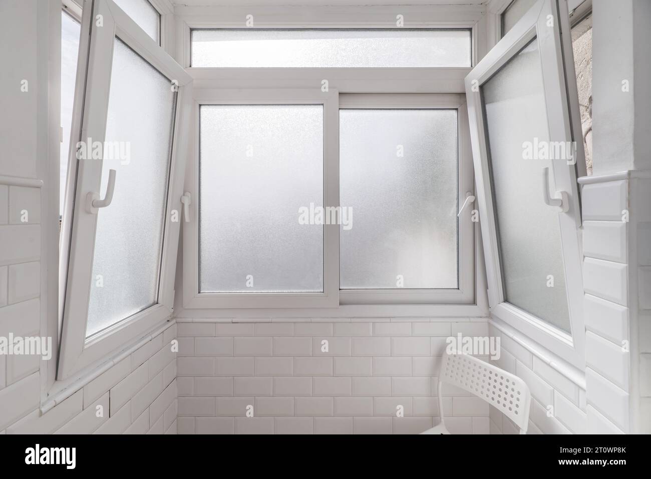 A small white tiled space with a chair of the same Stock Photo